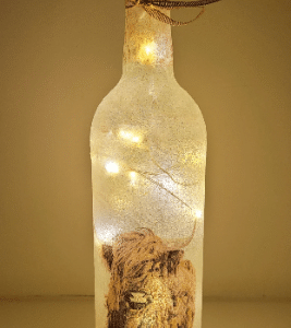 Standard wine bottle, lit up with a highland cow design. Cork LED lights and gold ribbon tied around the neck